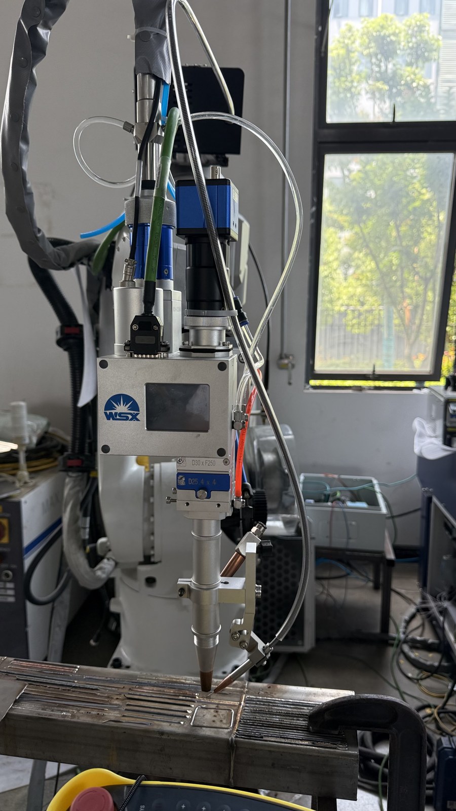 Robot-mounted laser welding head aligned near the metal workpiece